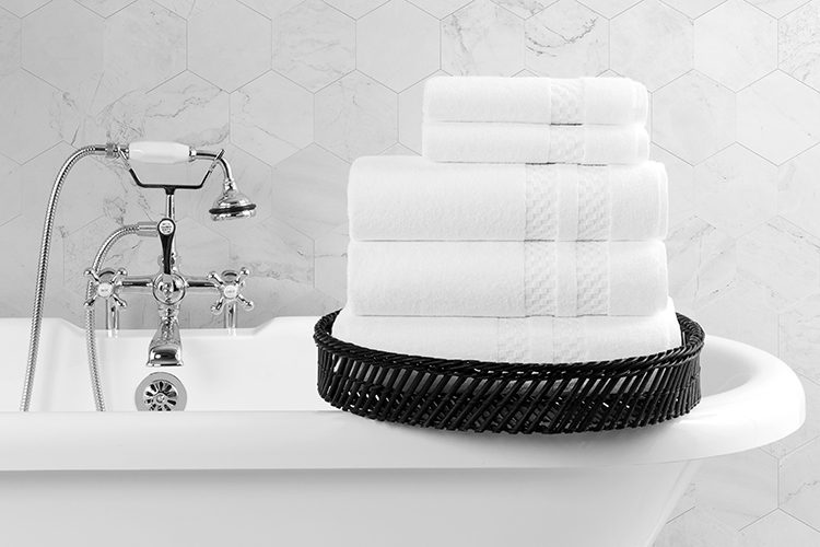 A stack of folded Capitol Bath Towels and Wash Cloths rest on the edge of an classic style clawfoot bath tub.
