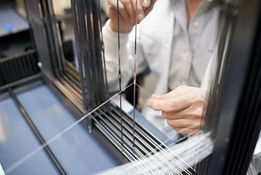 A close up image of a app team member threading yarn onto a weaving machine.